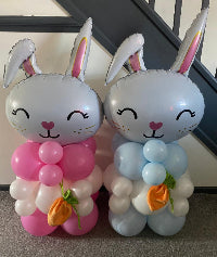Two custom easter balloons of rabbits in pink and blue with carrot decorations on a neutral background.